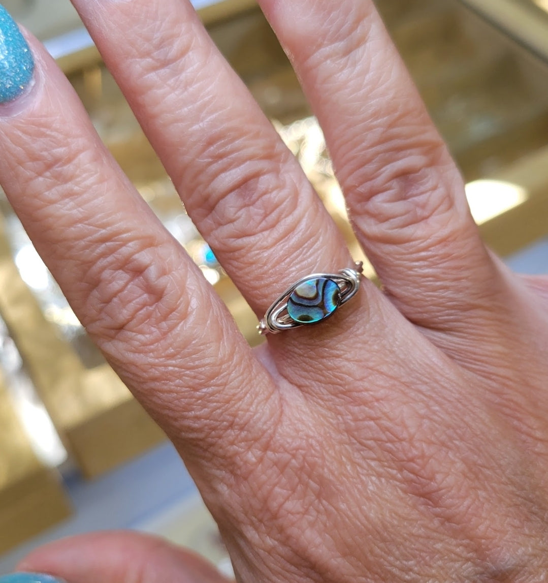 Sterling silver abalone wire-wrapped ring worn on the hand, showing iridescent shell colors