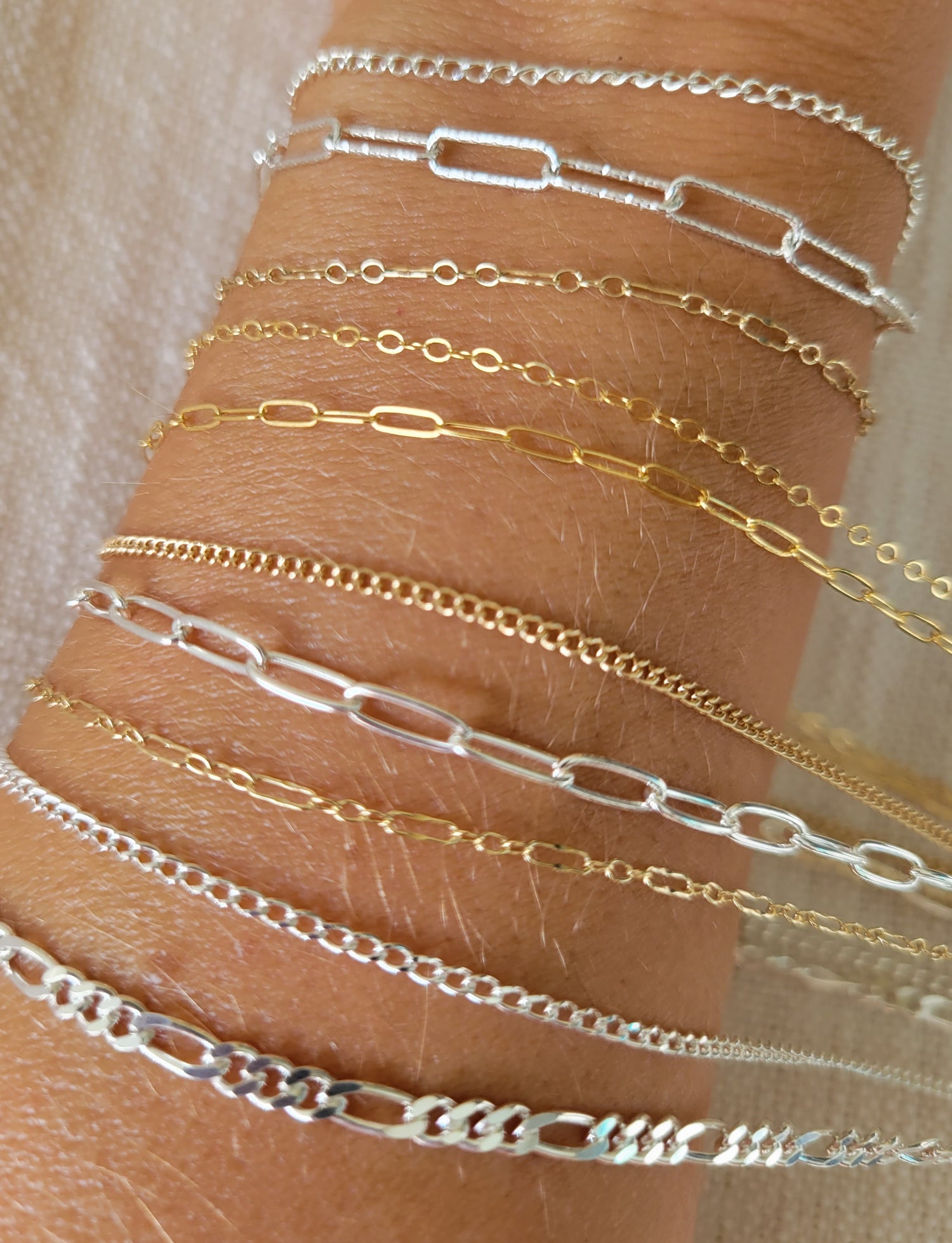 Permanent jewelry chains in sterling silver and 14k gold-filled displayed on wrist in Destin, Florida, featuring layered bracelet styles available locally