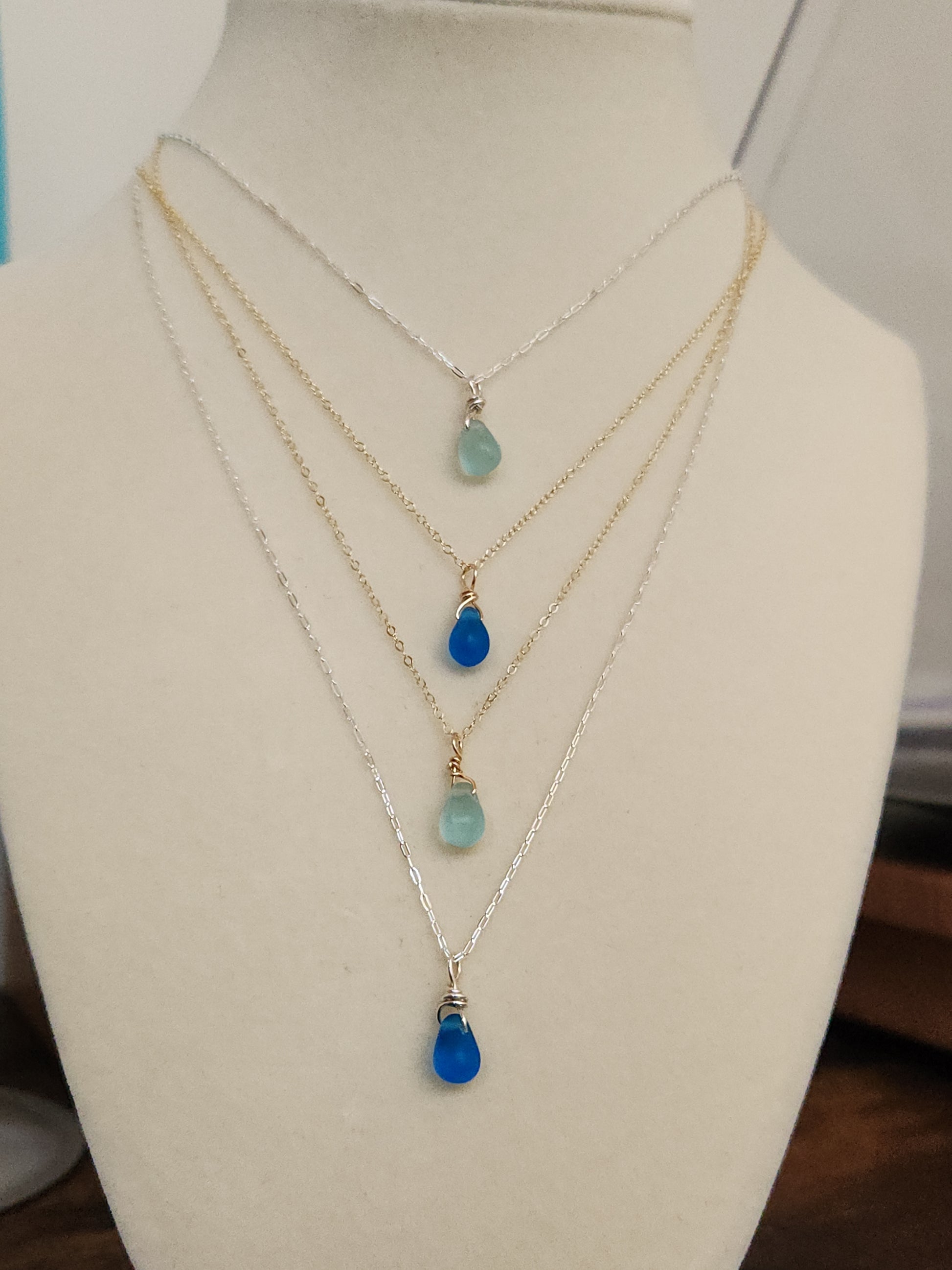 Two handcrafted sea glass necklaces layered, featuring light and dark blue glass pendants