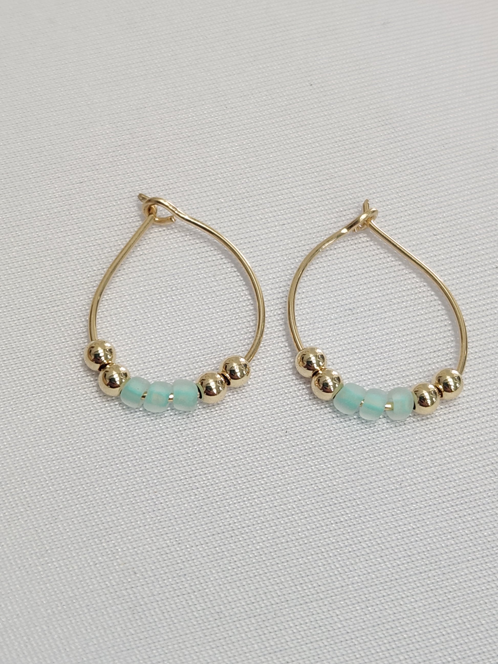 Front view of 14k gold-filled aqua hoop earrings with polished gold and glass bead accents