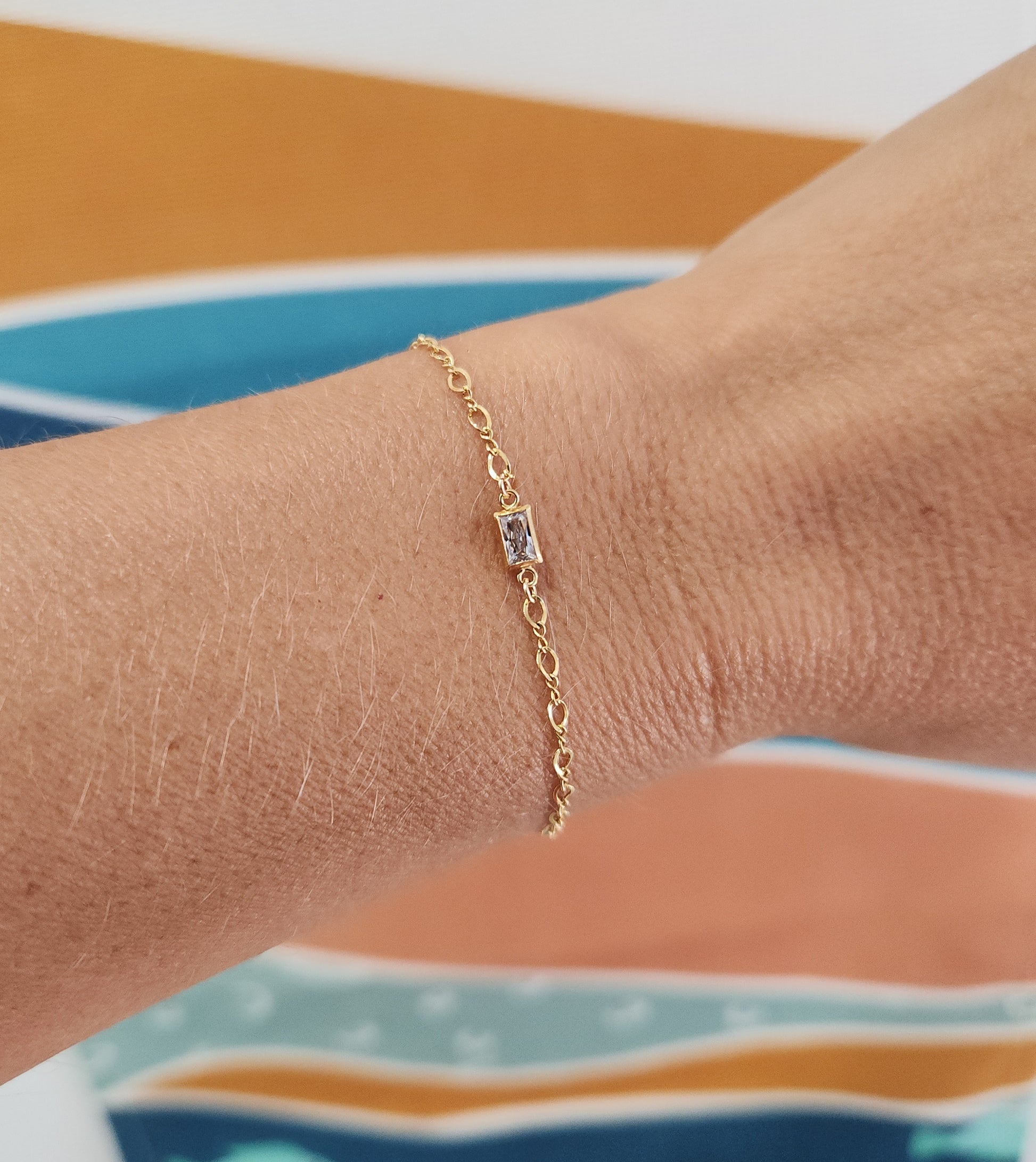 Gold-filled infinity chain bracelet featuring a diamond baguette centerpiece worn on the wrist