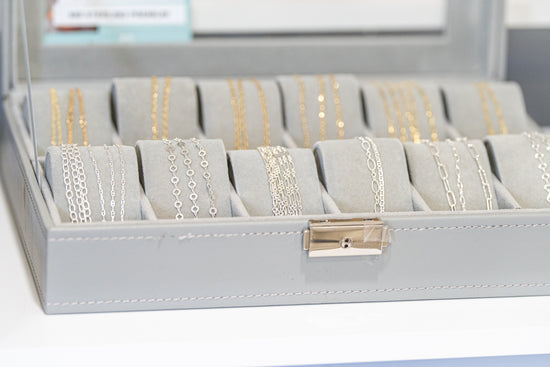 Mixed metal permanent jewelry chains displayed in a jewelry case, featuring sterling silver and gold-filled chain styles for customization