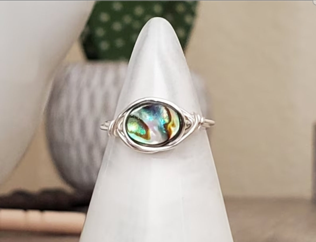 Ocean Glow abalone wire-wrapped ring handcrafted with sterling silver wire, displayed on a ring stand