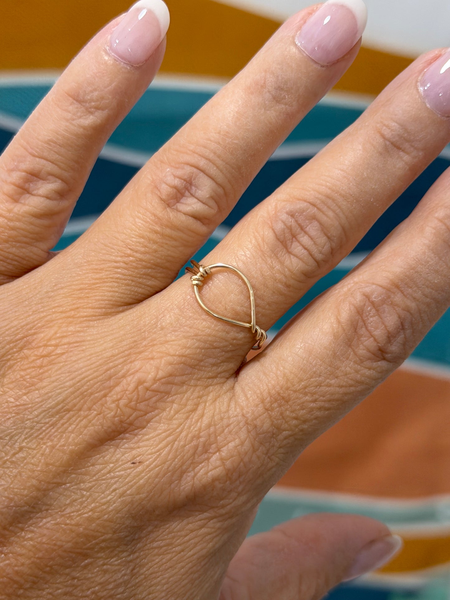 Minimalist gold-filled open-eye ring inspired by ocean waves displayed on a ceramic ring stand