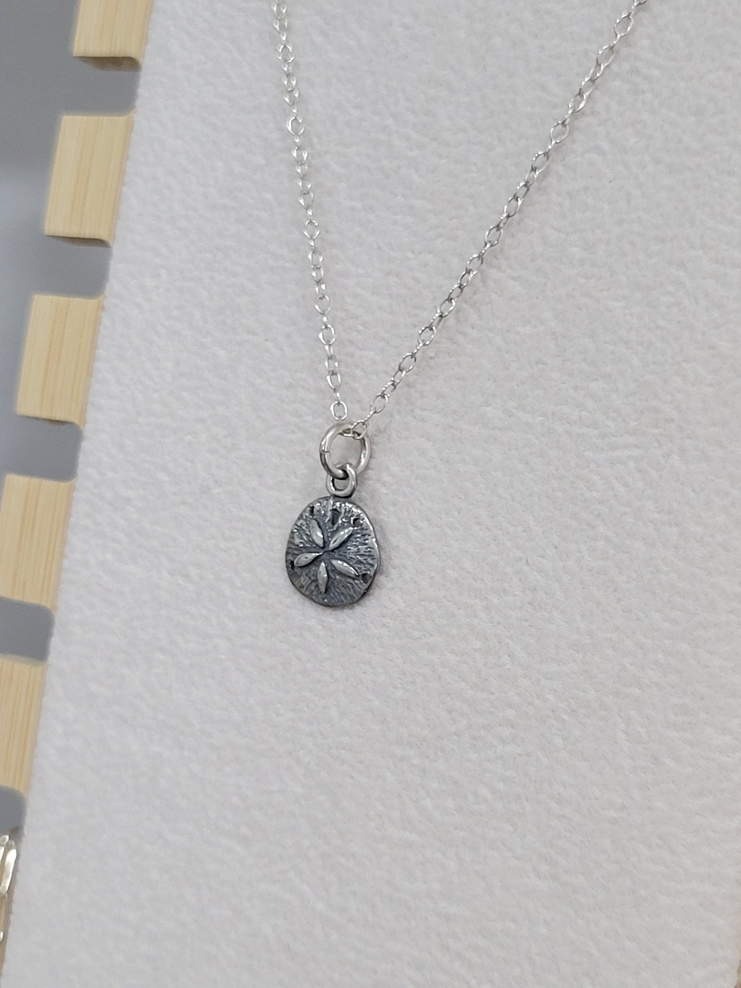 Close-up of sterling silver sand dollar charm necklace with detailed ocean texture