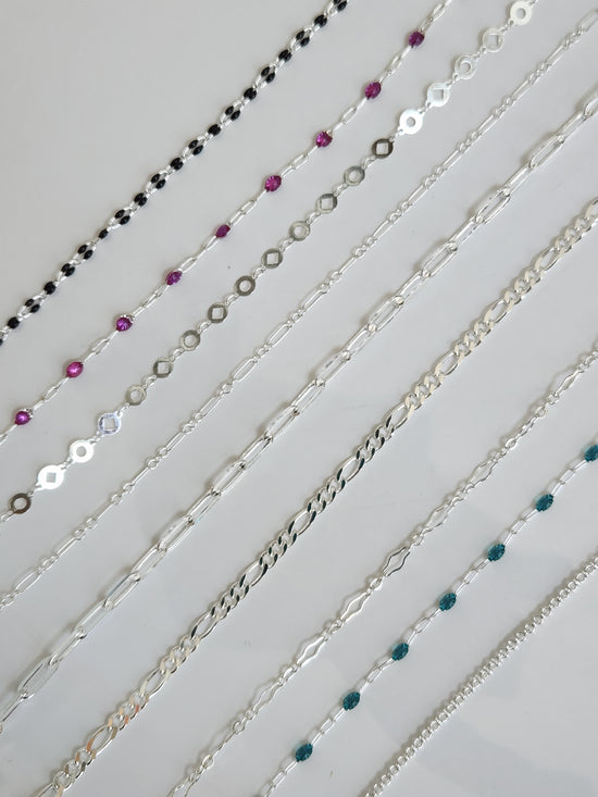 Selection of sterling silver permanent jewelry chains, including classic and colorful styles, displayed for customization